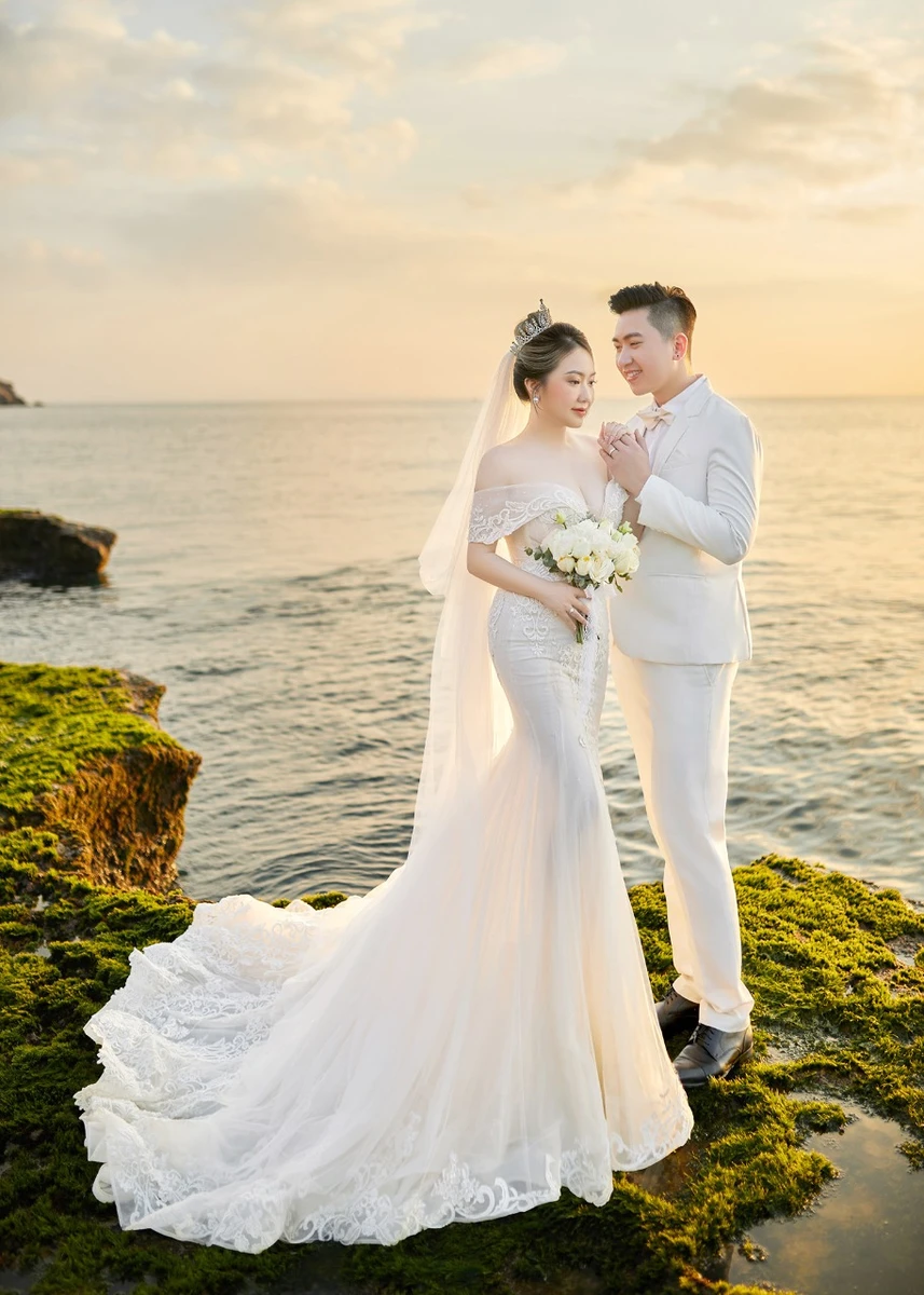 Cặp đôi rạng rỡ nắm tay nhau trên bãi đá rêu xanh lúc hoàng hôn
