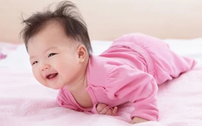 Trẻ sơ sinh mặc bộ đồ màu hồng đang nằm sấp ngẩng cao đầu vui vẻ trên đệm