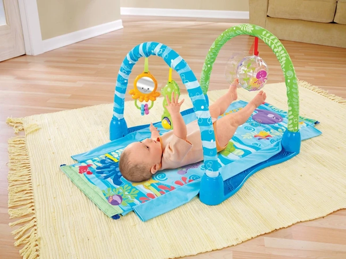 Em bé nằm ngửa, vui chơi vận động chân tay trên thảm với đồ chơi
