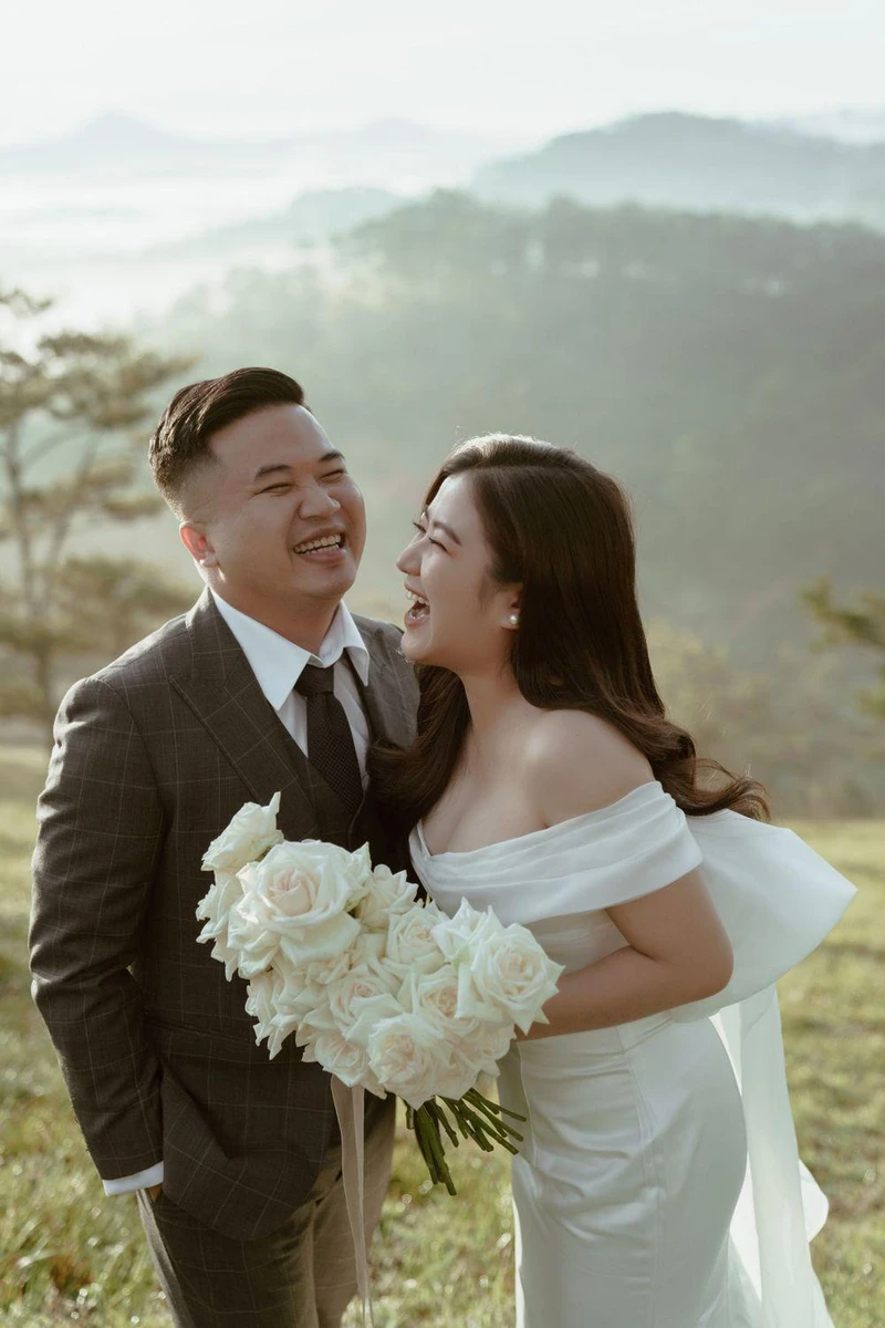 Cô dâu chú rể cùng bật cười, nghiêng người về phía nhau và ôm bó hoa lớn tạo khoảnh khắc chụp ảnh cưới tự nhiên
