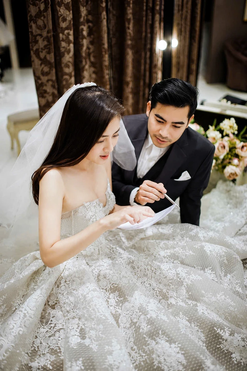 Cô dâu chú rể cùng ngồi xem tài liệu, chú rể nghiêng người quan sát còn cô dâu chỉ tay vào trang giấy tạo khoảnh khắc tự nhiên