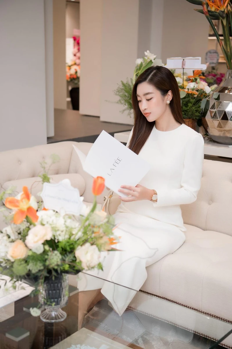 Cô gái diện váy trắng thanh lịch ngồi trên ghế sofa chăm chú xem cuốn catalogue