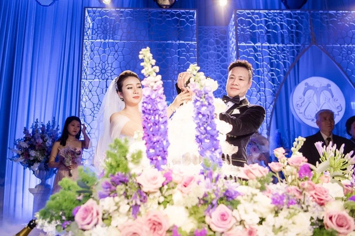 Cô dâu chú rể thực hiện nghi thức rót tháp ly champagne giữa không gian sân khấu cưới ngập tràn hoa tươi