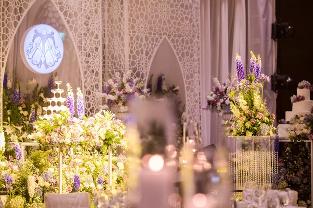 Toàn cảnh không gian tiệc cưới với sân khấu hoa tone tím, xanh pastel và trắng, kết hợp tháp ly champagne sang trọng