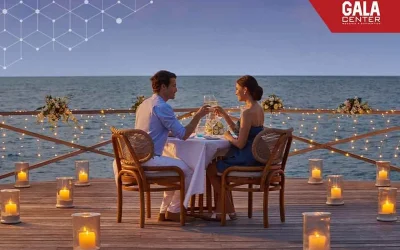 Cặp đôi thưởng thức bữa tối lãng mạn bên bờ biển trong tuần trăng mật với khung cảnh hoàng hôn và ánh nến