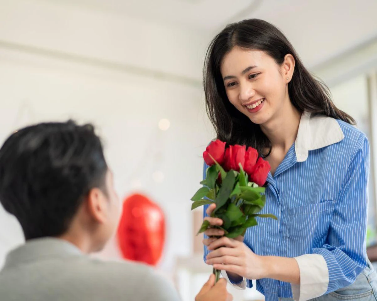 Cô gái mỉm cười rạng rỡ khi nhận bó hoa hồng đỏ từ người yêu, thể hiện niềm vui và hạnh phúc trọn vẹn khi được yêu thương
