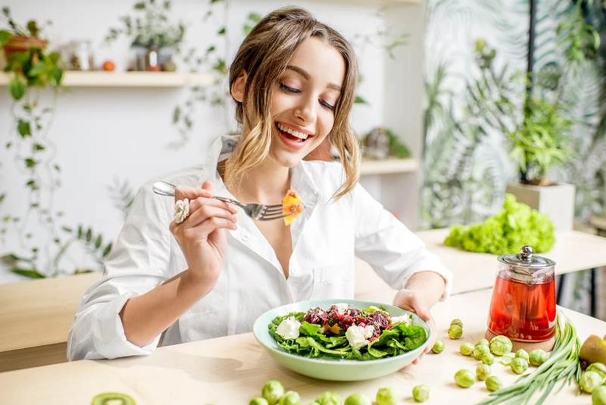 Cô gái trẻ mỉm cười rạng rỡ khi thưởng thức đĩa salad tươi ngon, tại bàn ăn
