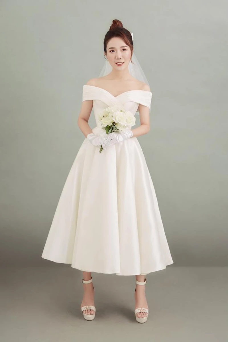 Đầm midi cổ điển trễ vai, dáng xoè thanh lịch, tay cầm bó hoa trắng nhẹ nhàng