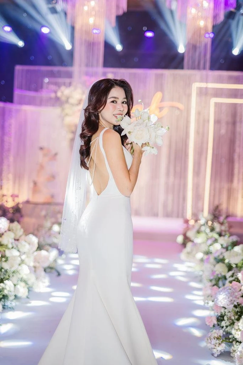 Cô dâu diện váy cưới hở lưng với voan trắng dài trên tay là bó hoa cưới màu trắng
