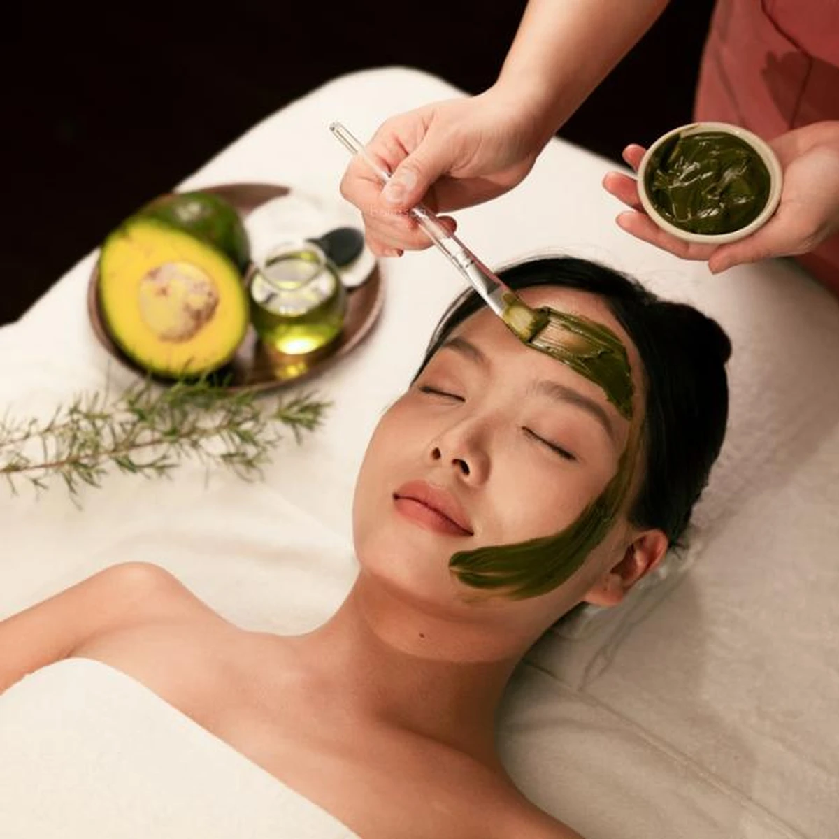 Cô gái đang thư giãn khi được nhân viên thoa mặt nạ bơ lên trán