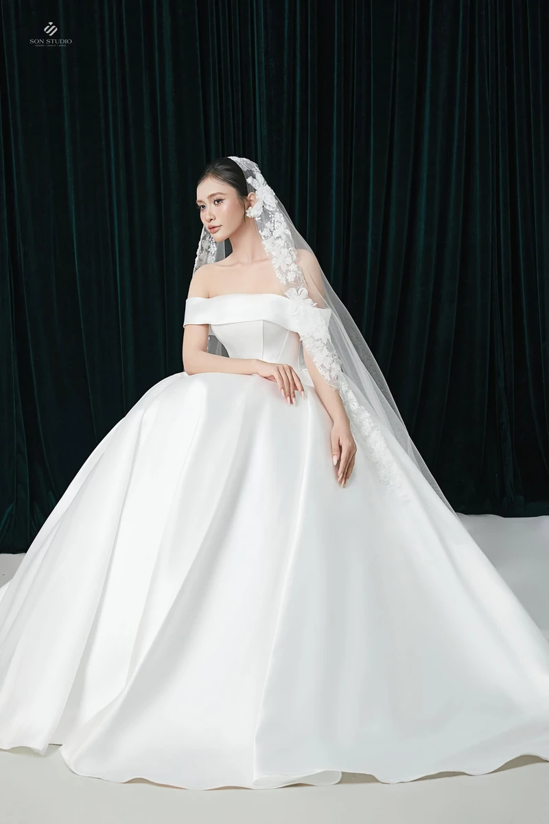Cô dâu mặc trên người váy cưới trễ vai, vải satin phối cùng voan thêu hoa nổi
