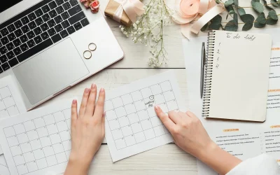 Góc nhìn từ trên xuống bàn làm việc có máy tính, nhẫn cưới và bàn tay đang chỉ ngày cưới trên tờ lịch