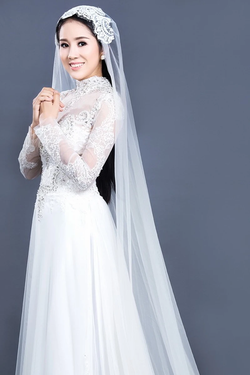 Cô dâu mặc áo dài cưới trắng ren cổ cao tay dài, kết hợp khăn voan dài và phụ kiện ren cài đầu