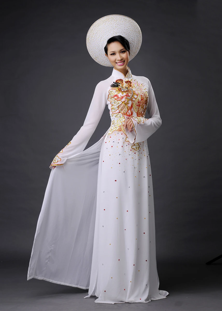 Cô dâu mặc áo dài cưới trắng với hoạ tiết thêu vàng đỏ nổi bật kết hợp đội mấn truyền thống cùng kiểu tóc búi gọn tạo vẻ đẹp sang trọng