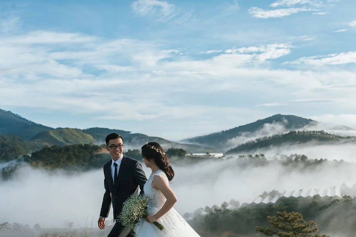 Khung cảnh chụp ảnh cưới siêu đẹp trên đỉnh núi cao lộng gió, cô dâu cầm bó hoa cưới cùng chú rể dạo bước giữa biển mây trắng xóa bao phủ thung lũng