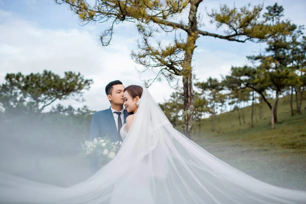 Chú rể nhẹ nhàng đặt nụ hôn lên trán cô dâu dưới bóng cây thông cô đơn, tà khăn voan cưới trắng bay bổng nhẹ nhàng trong gió núi